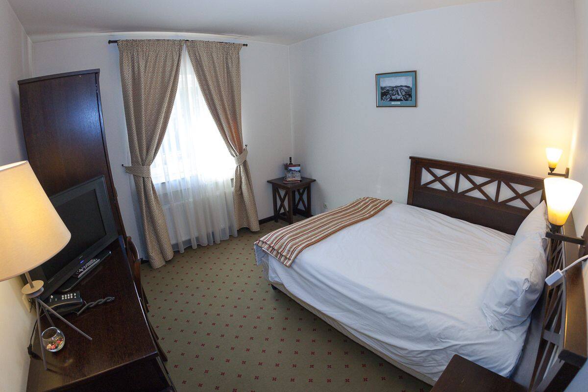 A hotel room with a bed, a TV, a lamp, a small table, and a picture on the wall.