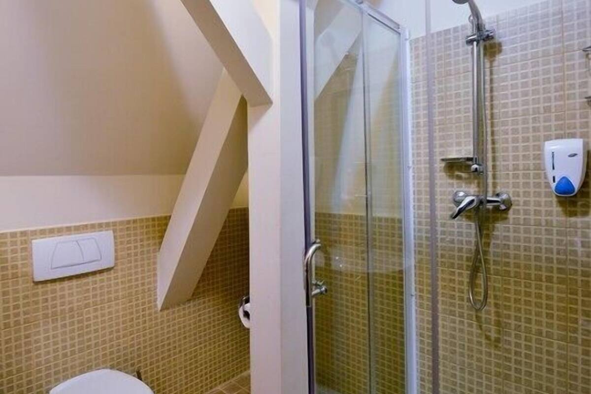 A bathroom with a glass-enclosed shower, a toilet, and a hand soap dispenser on the wall.