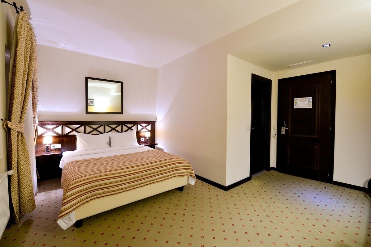 A hotel room with a bed, a nightstand, a lamp, and a door.