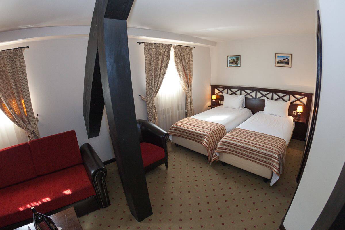 A hotel room with a bed, a red sofa, and a chair.