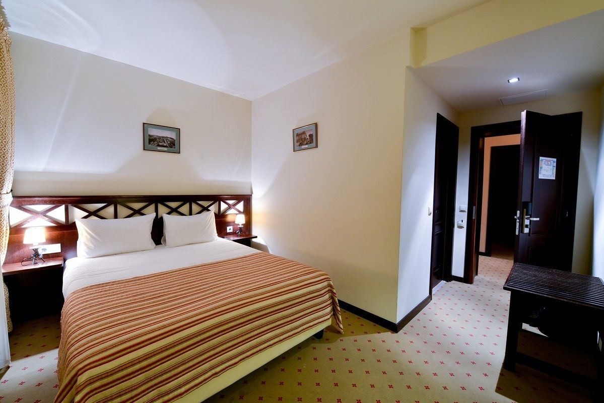 Une chambre d’hôtel avec un grand lit, une tête de lit en bois, deux tables de chevet avec des lampes et un petit bureau avec une chaise.