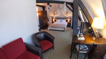 Een hotelkamer met een hemelbed, een bureau met een lamp, een rode bank en een houten garderobe.