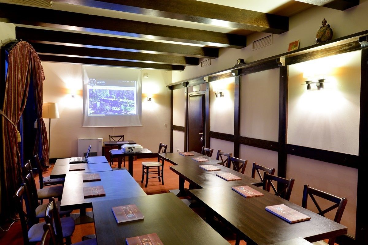 A conference room with long tables, chairs, a projector screen, and a large window.