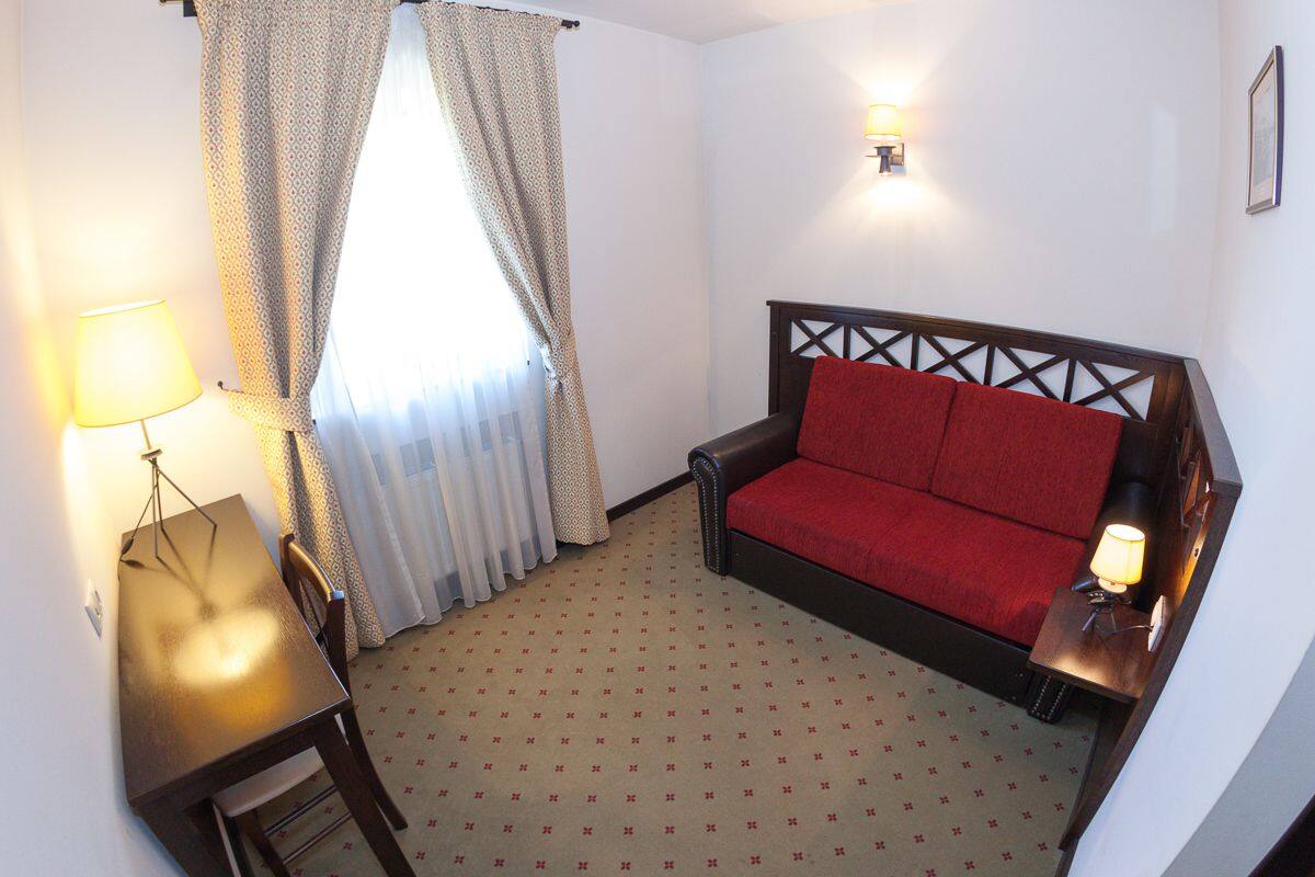 A small room with a red sofa, a wooden table, a lamp, and a window with curtains.