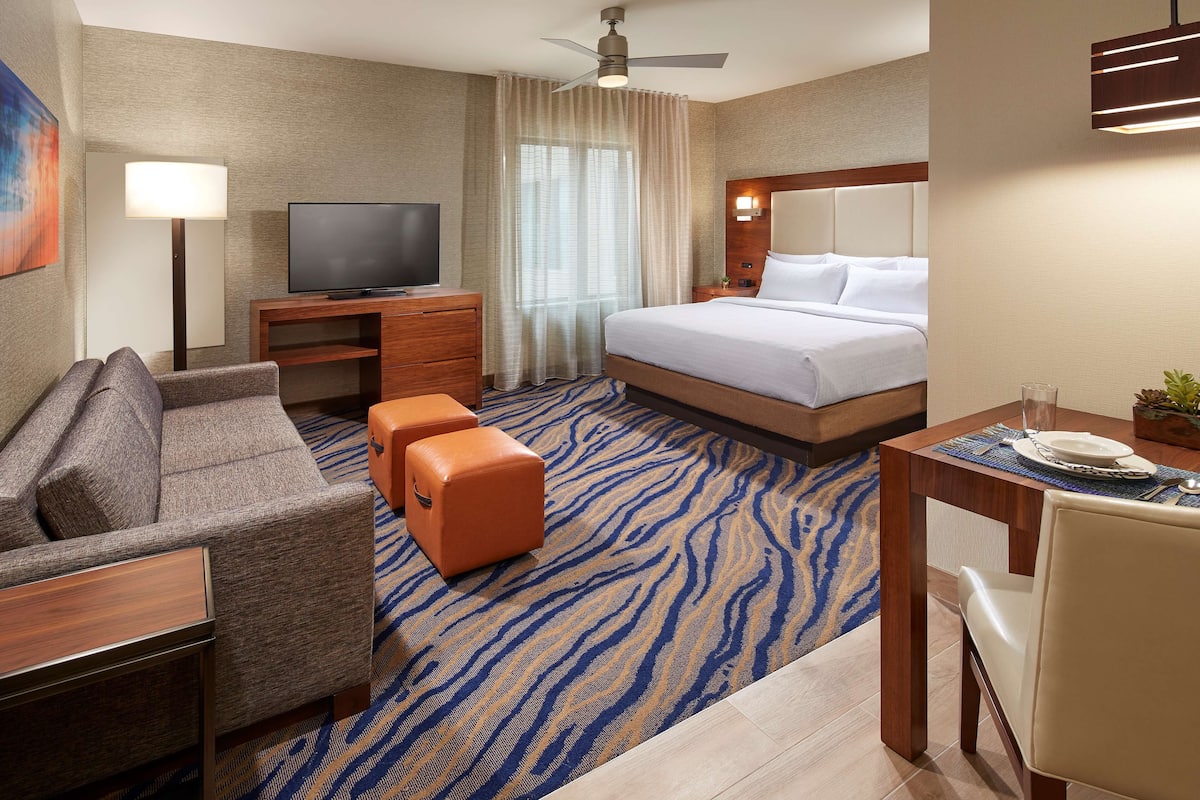 A hotel room with a bed, a TV, a sofa, an ottoman, a desk, and a dining table.