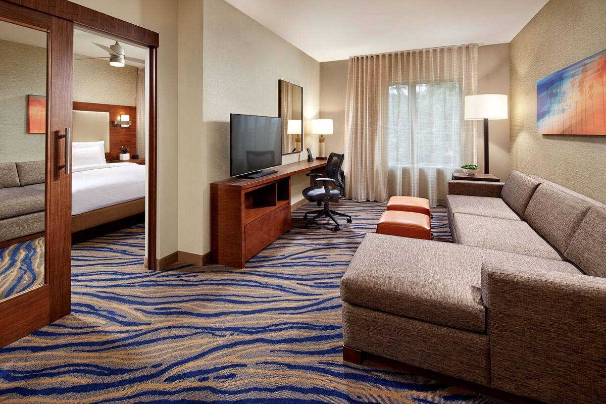 A hotel room with a bed, a TV, a sofa, a desk, and a chair.