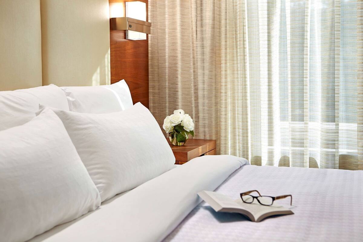 A hotel room with a neatly made bed, a bedside table with a vase of flowers, and a window with curtains.