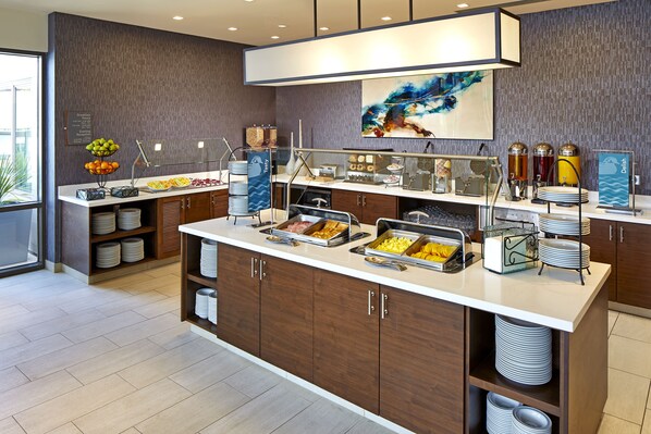 A buffet setup with various food items, a coffee station, and a decorative wall piece.