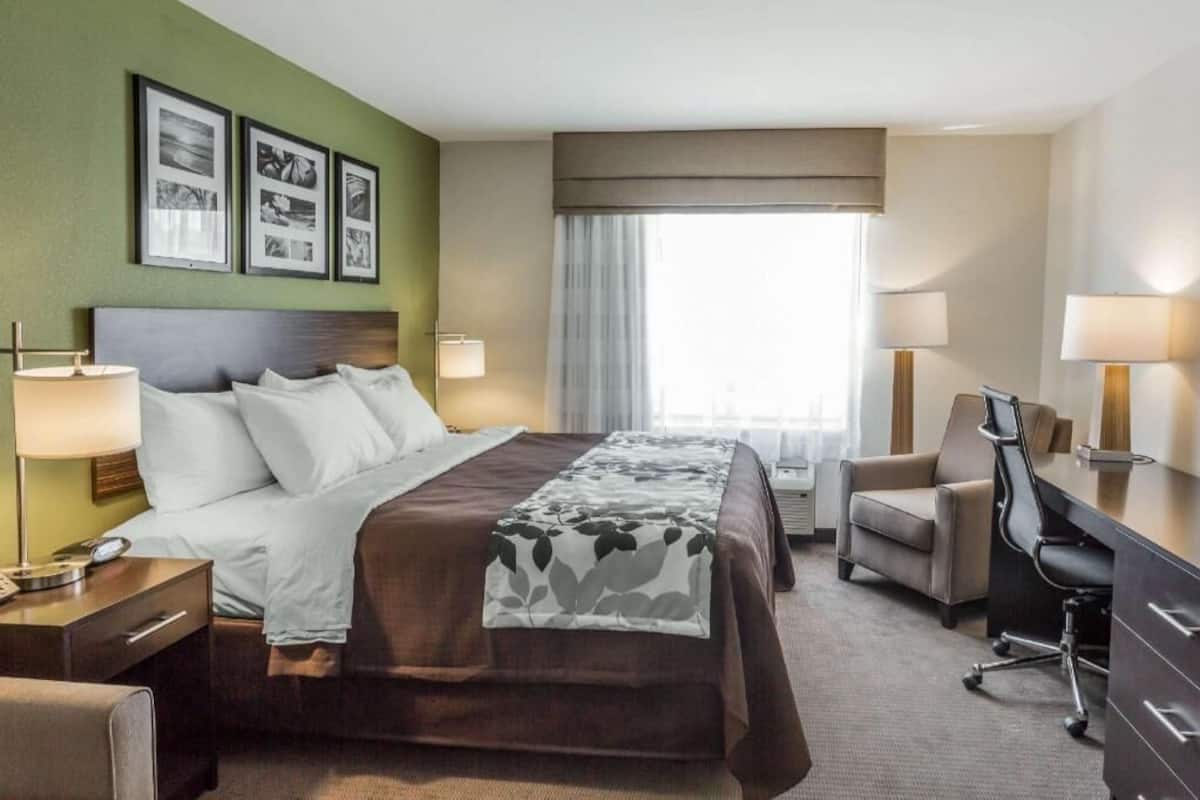 A hotel room with a bed, bedside tables, a desk, a chair, and a window with curtains.