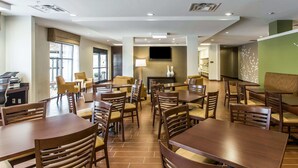 A hotel dining area with multiple wooden tables and chairs, a flat-screen TV mounted on the wall, and a fireplace. - Sleep Inn & Suites Dayton South (Dayton)