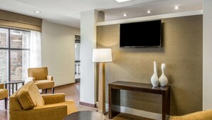 A hotel lobby with a flat-screen TV mounted on the wall, a sofa, a coffee table, and a lamp. - Sleep Inn & Suites Dayton South (Dayton)