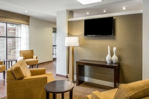 Un vestíbulo de hotel con una televisión de pantalla plana montada en la pared, un sofá, una mesa de centro y una lámpara.