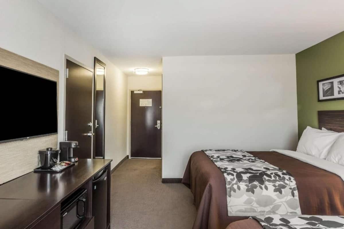 A hotel room with a bed, a television, a desk with a coffee maker, and a door leading to another room.