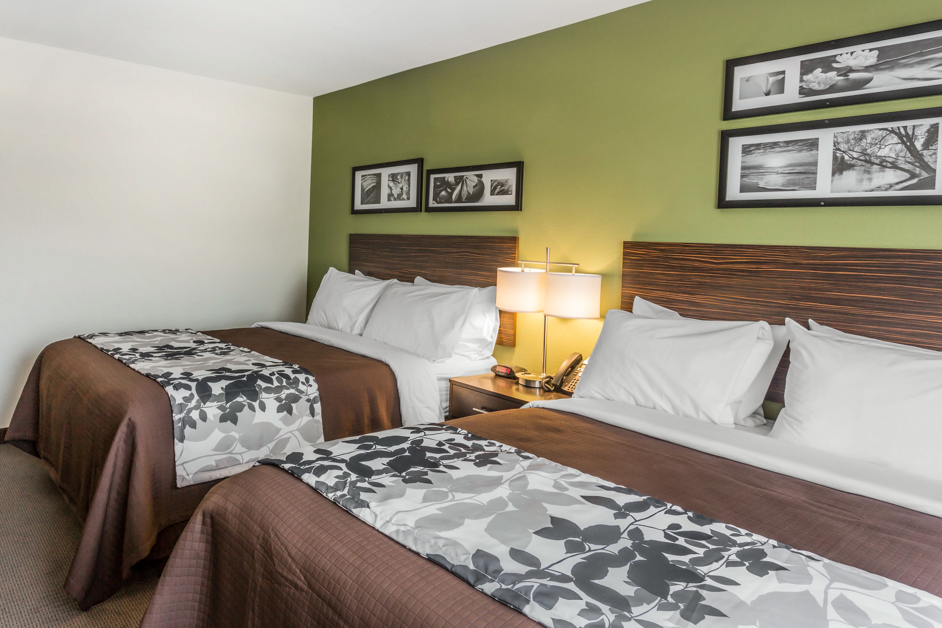 A hotel room with two beds, a nightstand with a lamp, and framed pictures on the wall.