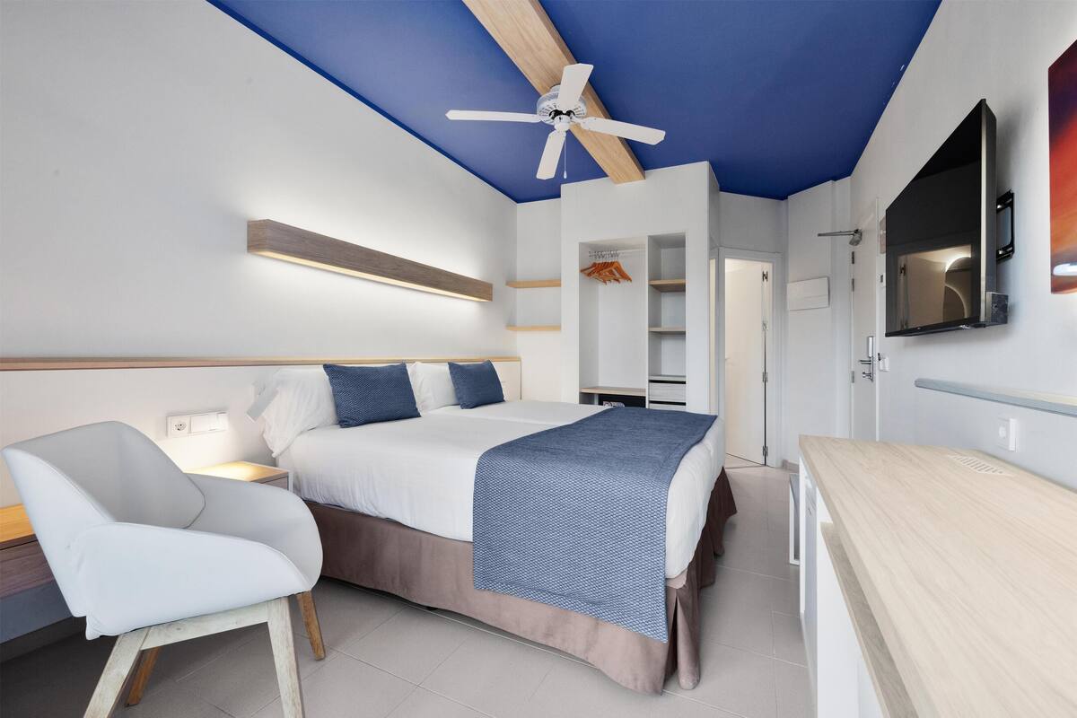Une chambre moderne avec un lit, une table de chevet, une chaise et un ventilateur de plafond.