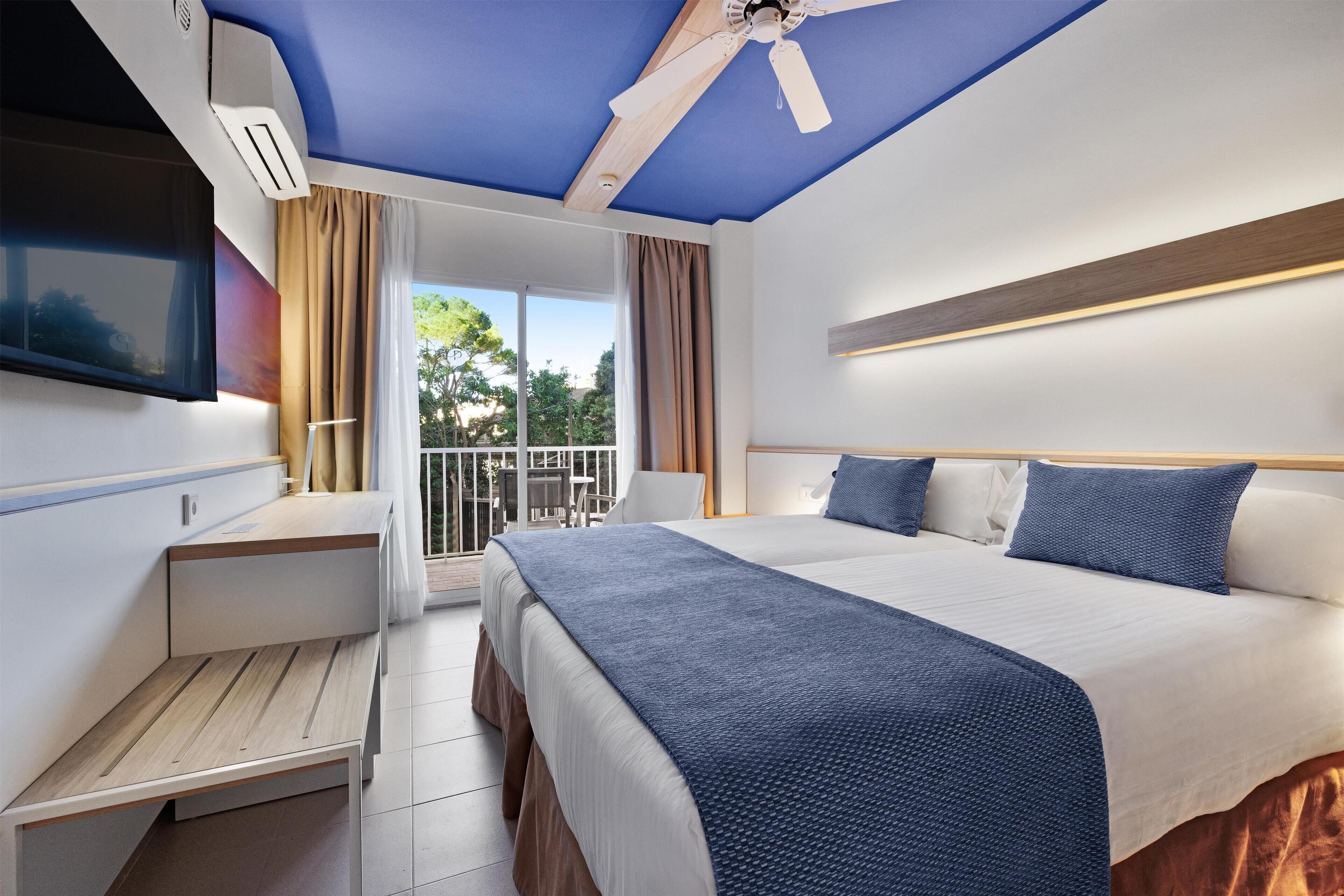 Quarto de hotel moderno com uma cama grande, uma escrivaninha e um ventilador de teto.
