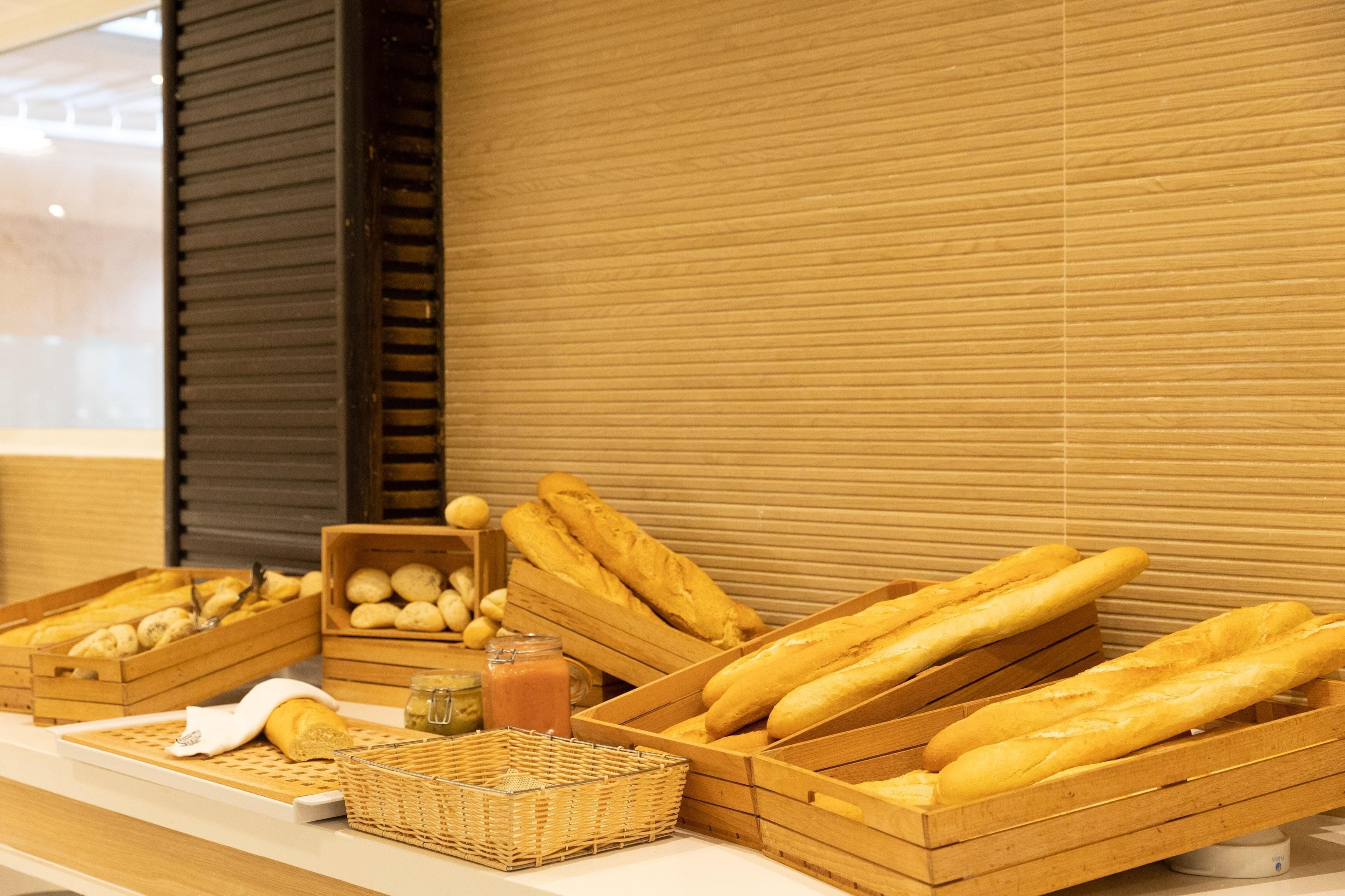 A display of bread and pastries in wooden crates, a wicker basket, and a jar of jam.