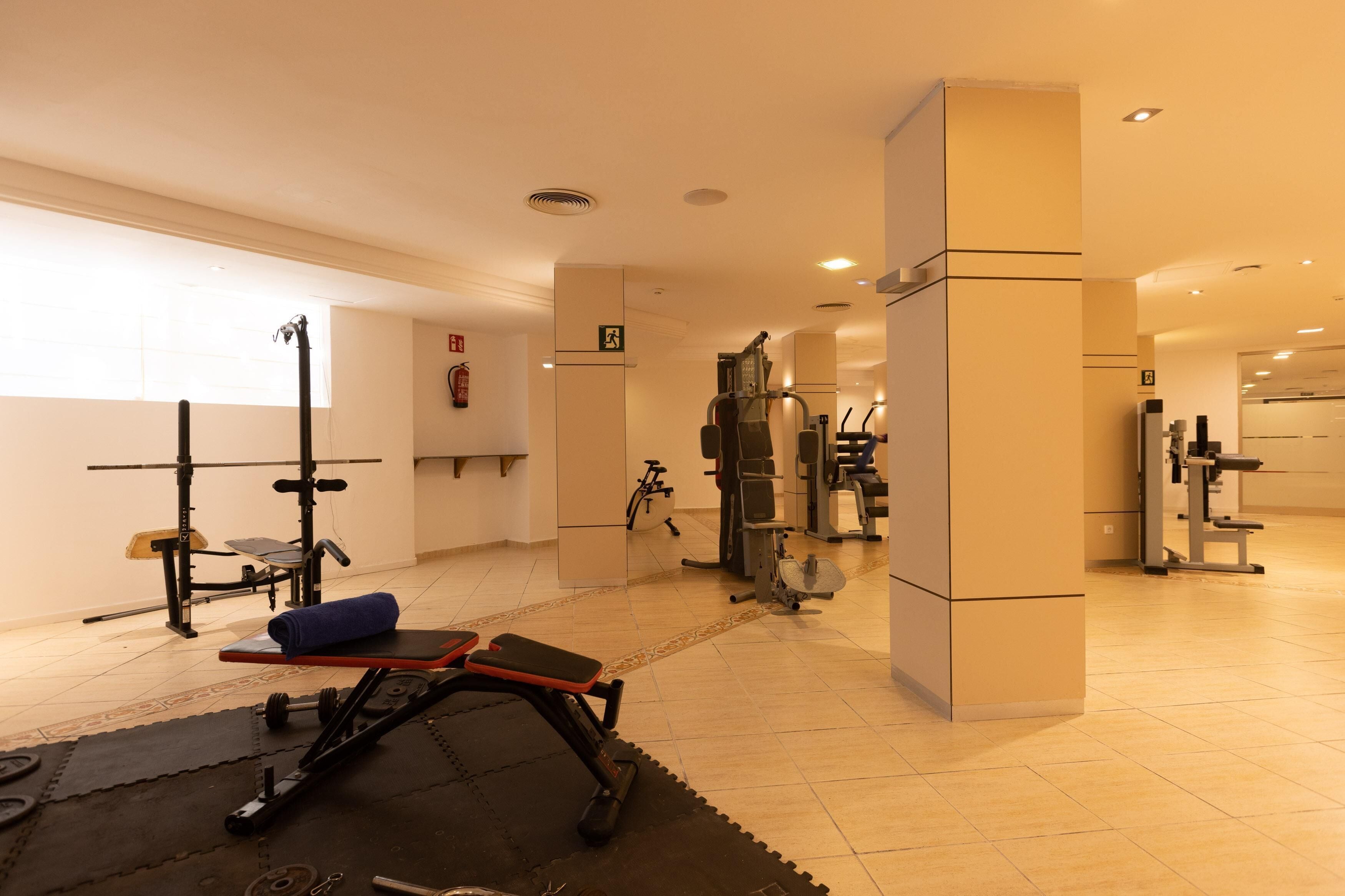 Un gimnasio con diversos equipos de ejercicio, incluyendo una prensa de banca, una jaula para sentadillas y cintas de correr.