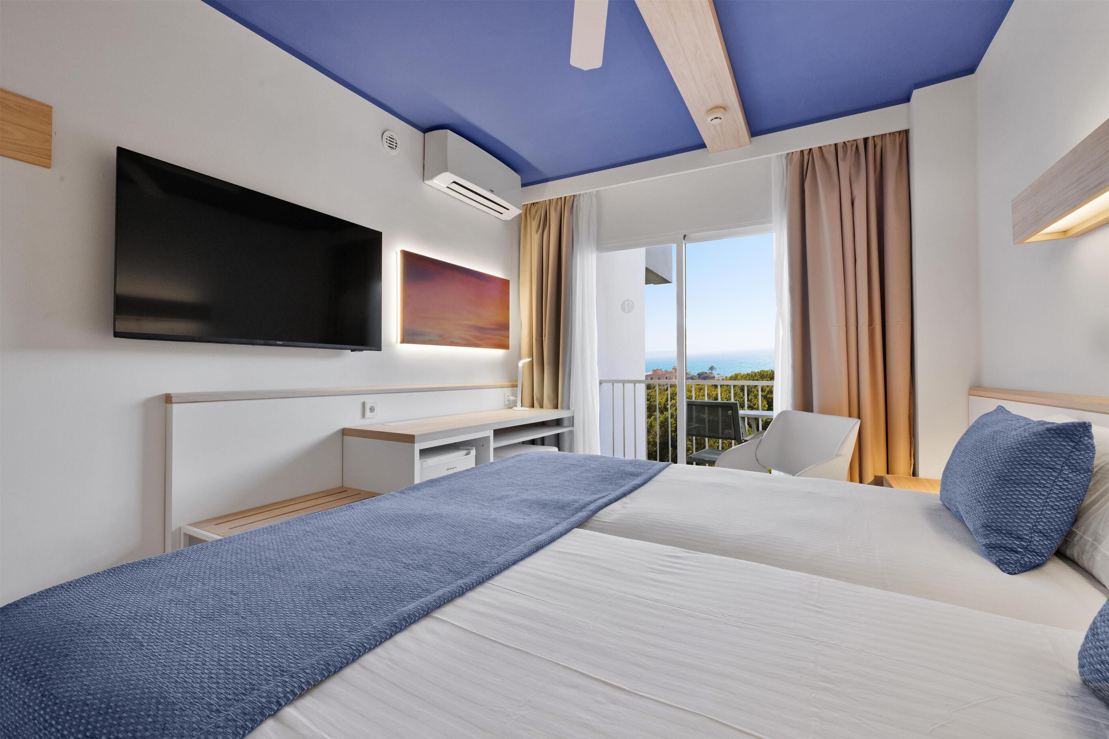 Une chambre d’hôtel dotée d’un grand lit, d’un téléviseur à écran plat fixé au mur, d’un bureau avec une chaise et d’un balcon offrant une vue agréable.