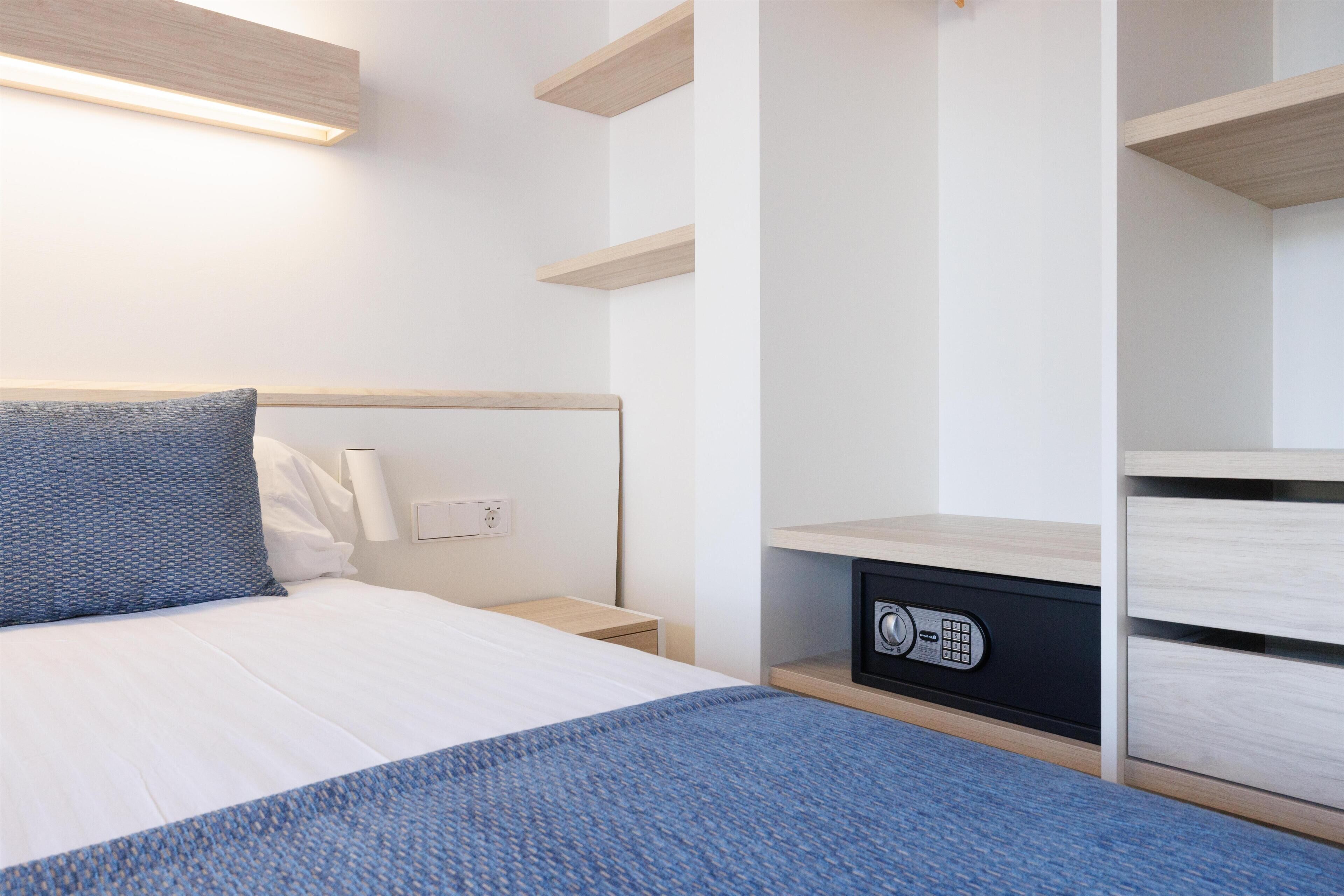 Una habitación de hotel moderna con cama, mesitas de noche, una caja fuerte integrada y un armario con puertas correderas.