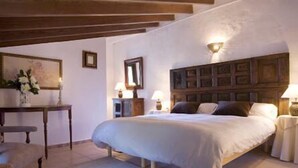 A bedroom with a large bed, a wooden headboard, a bedside table with a lamp, and a small table with a vase of flowers. - Vall de Pollença (Pollenca)