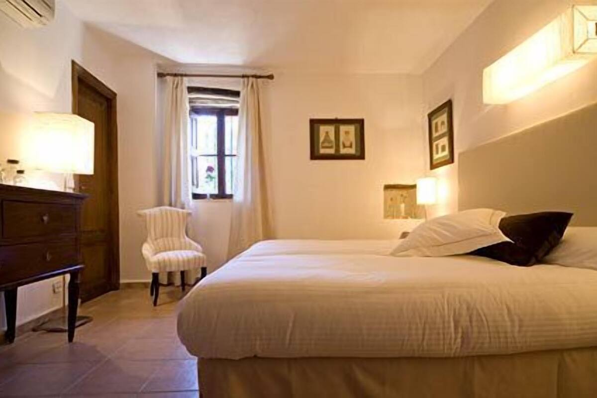 A hotel room with a bed, a chair, a dresser, and a window with curtains.