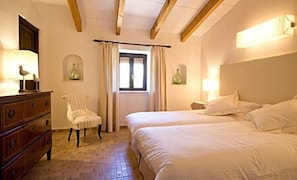 A hotel room with a wooden dresser, a chair, a bed with white linens, and a window with curtains. - Vall de Pollença (Pollenca)