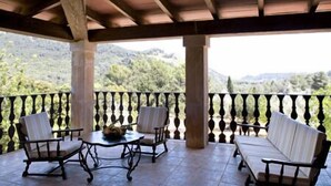 A covered outdoor seating area with two sofas and two chairs, a table with a bowl, and a view of a mountainous landscape. - Vall de Pollença (Pollenca)