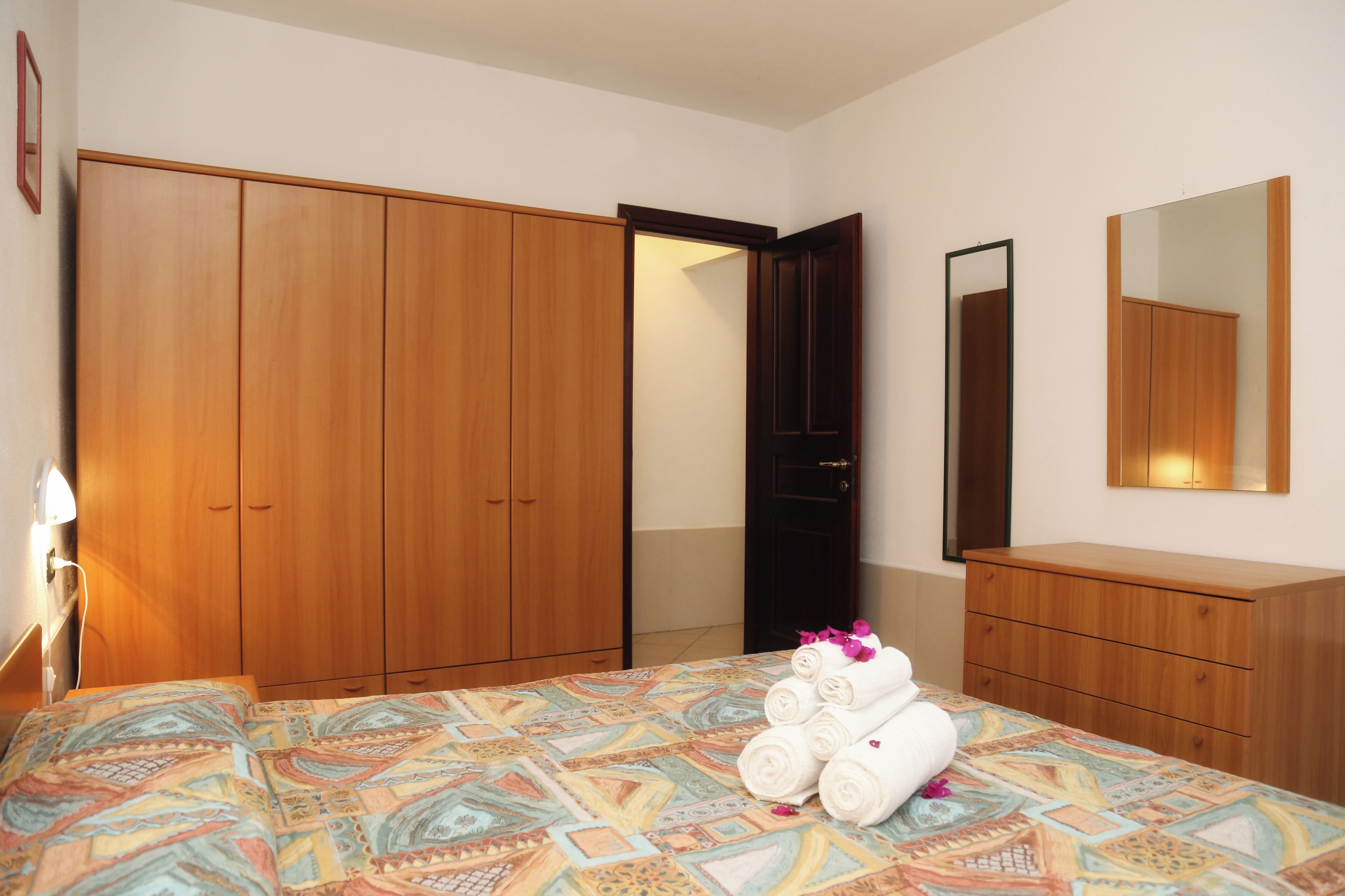 Une chambre d’hôtel avec un lit, une armoire en bois, une commode et un miroir.