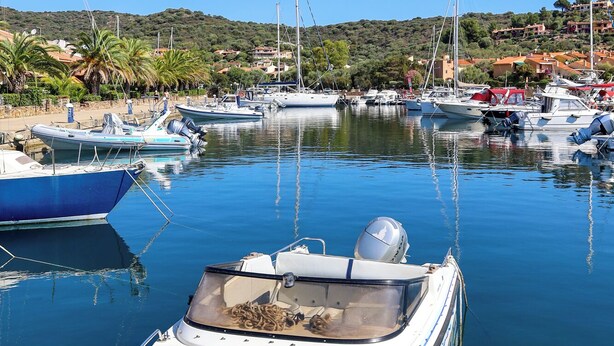 Eine Marina mit mehreren angestaubten Booten, einem klaren blauen Himmel und einer hügeligen Landschaft im Hintergrund.