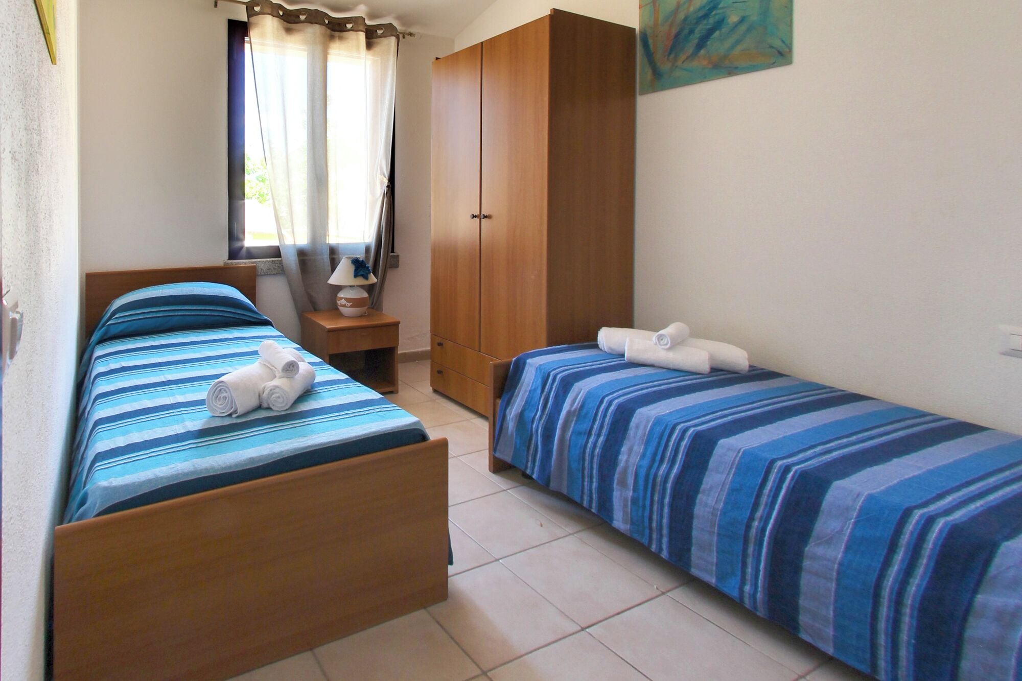 A bedroom with two beds, a wardrobe, a nightstand, and a window with curtains.