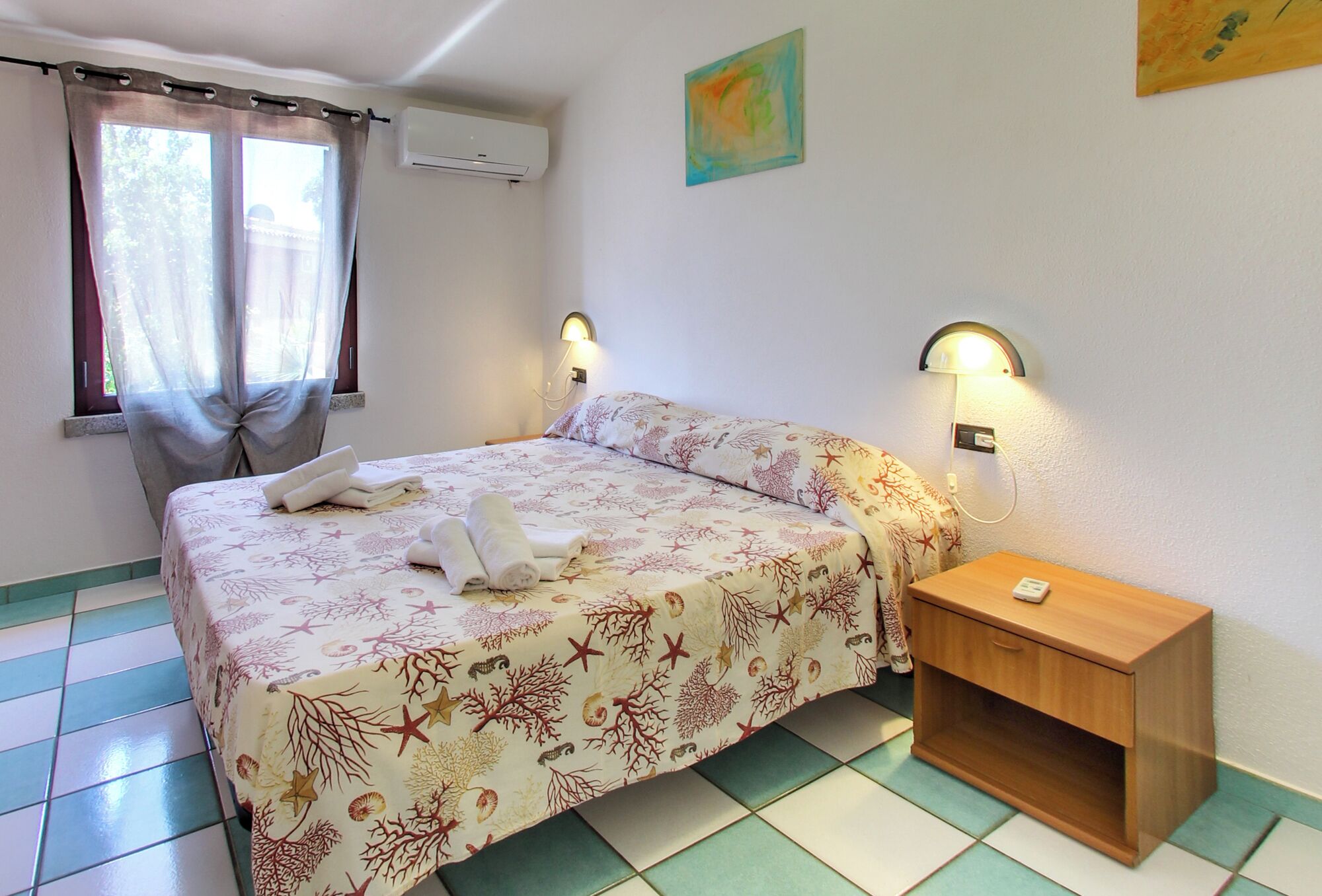A bedroom with a bed, a nightstand, a wall-mounted lamp, and a window with curtains.