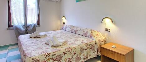 A bedroom with a bed, a nightstand, a wall-mounted lamp, and a window with curtains.
