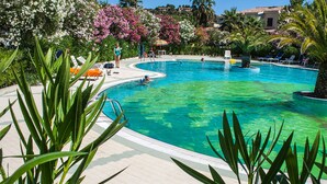 Ein Pool mit gewölbter Kante, umgeben von Liegestühlen und Palmen.