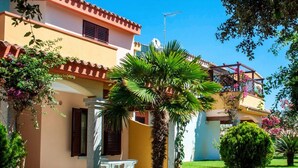 Eine mediterrane Villa mit gefliestem Patio, einer Palme sowie einem kleinen Tisch und Stühlen.