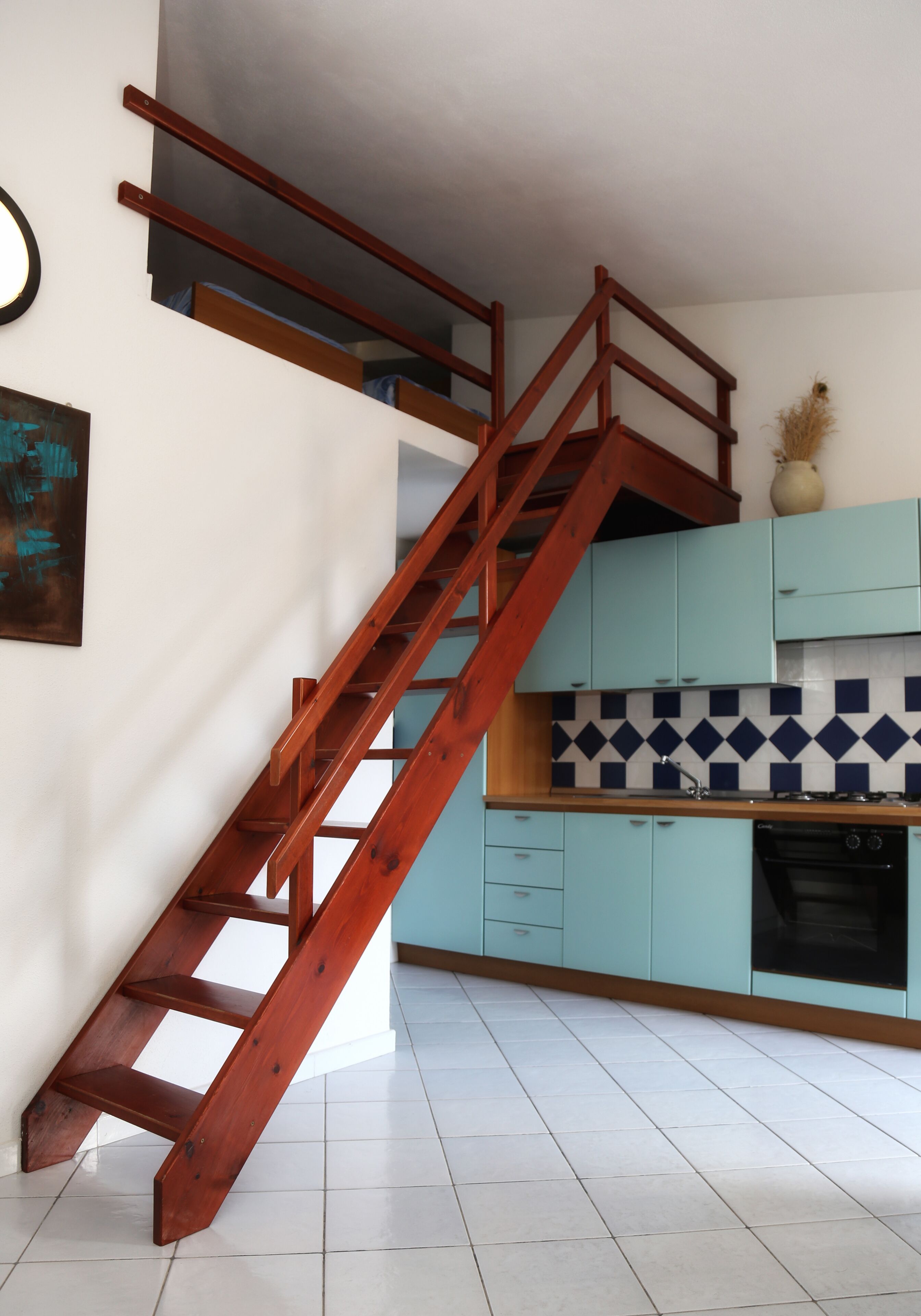 A kitchen with teal cabinets, a tiled backsplash, and a wooden staircase.