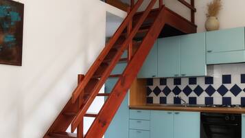 A kitchen with teal cabinets, a tiled backsplash, and a wooden staircase.