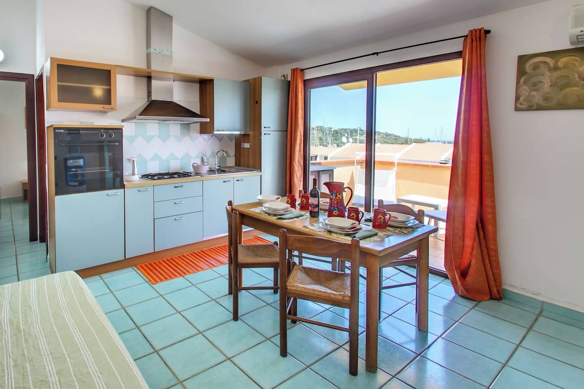 A compact kitchen with a dining area, a large window with curtains, and a view of the landscape.