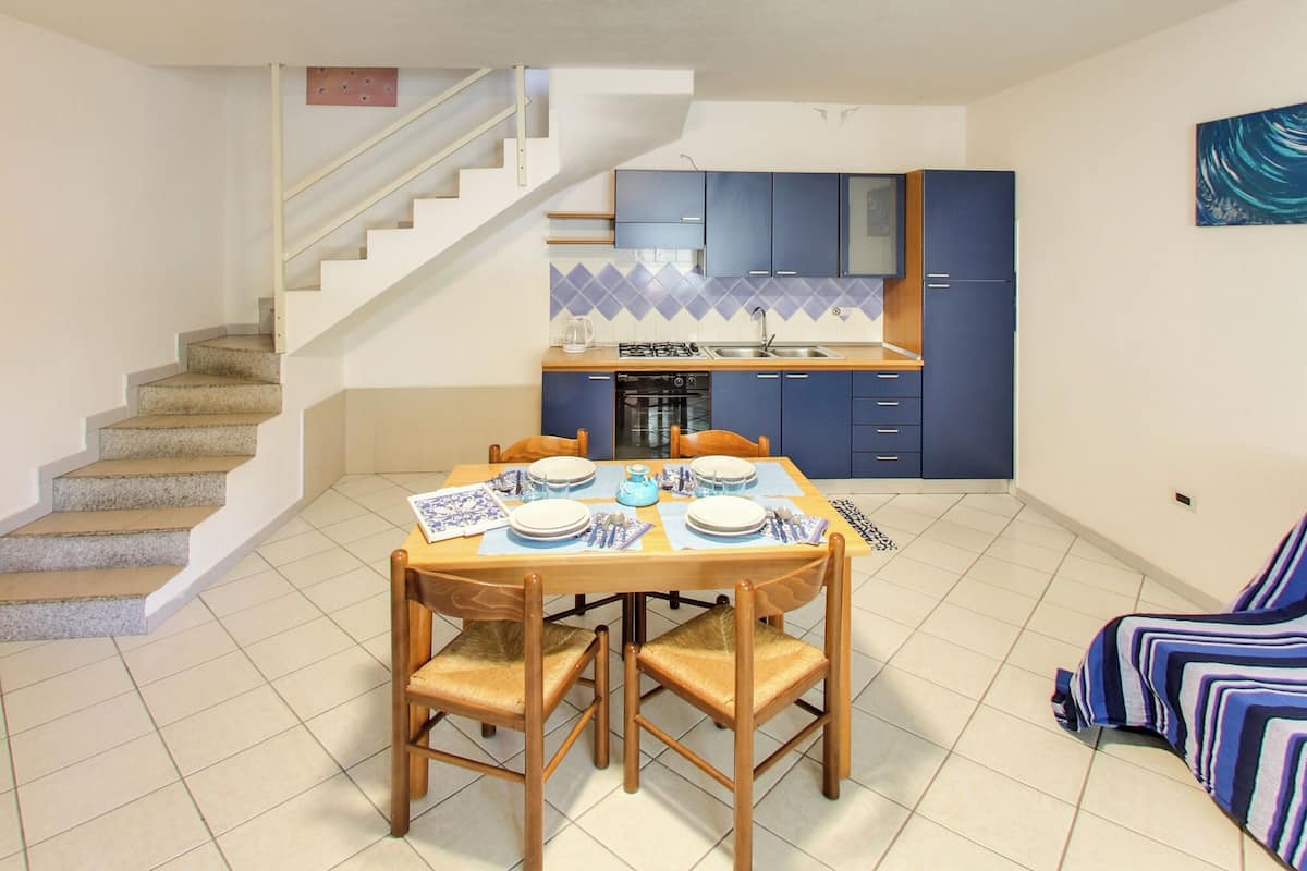 A dining area with a table set for four, a kitchen with blue cabinets, and a staircase leading to an upper floor.