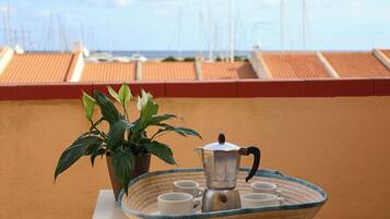 Una terraza con espacio para café, que incluye un recipiente metálico y tazas, además de una planta en maceta.