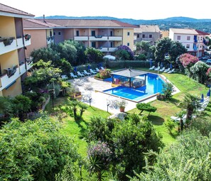 A hotel with a swimming pool, outdoor seating, and lush greenery. - Residence Li Velieri (Santa Teresa di Gallura)