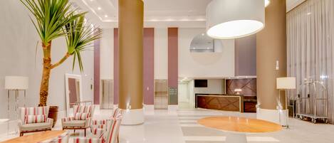 A spacious lobby with a reception desk, seating area, and a large plant.