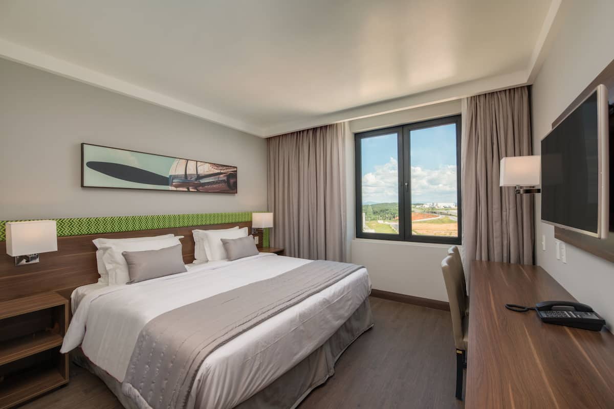 Habitación de hotel con una cama grande, un escritorio con teléfono, una televisión y una ventana con vistas al exterior.