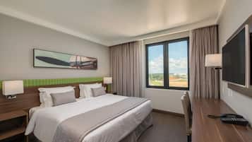 Habitación de hotel con una cama grande, un escritorio con teléfono, una televisión y una ventana con vistas al exterior.