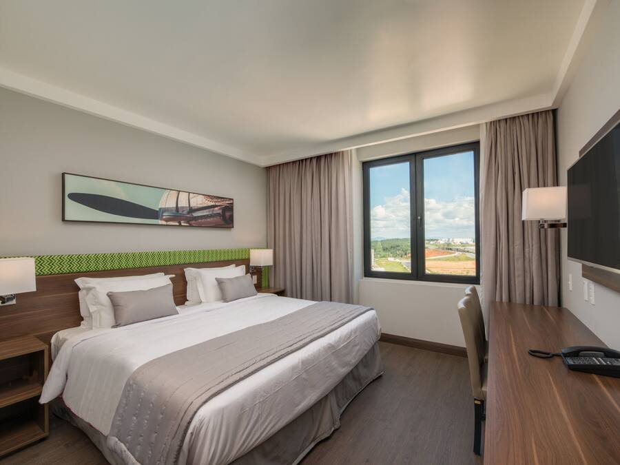 Habitación de hotel con una cama grande, un escritorio con teléfono, una televisión y una ventana con vistas al exterior.