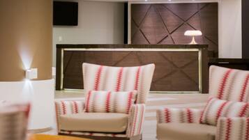 A modern lobby with a reception desk, two armchairs, and a wall-mounted TV.