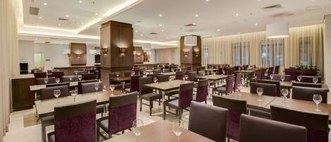 A spacious hotel dining area with multiple tables and chairs, equipped with wine glasses.