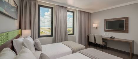 Habitación de hotel con dos camas, un escritorio, una silla, un televisor y ventana con vista a la ciudad.