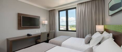 Habitación de hotel con dos camas, un escritorio, un televisor y una ventana con cortinas.
