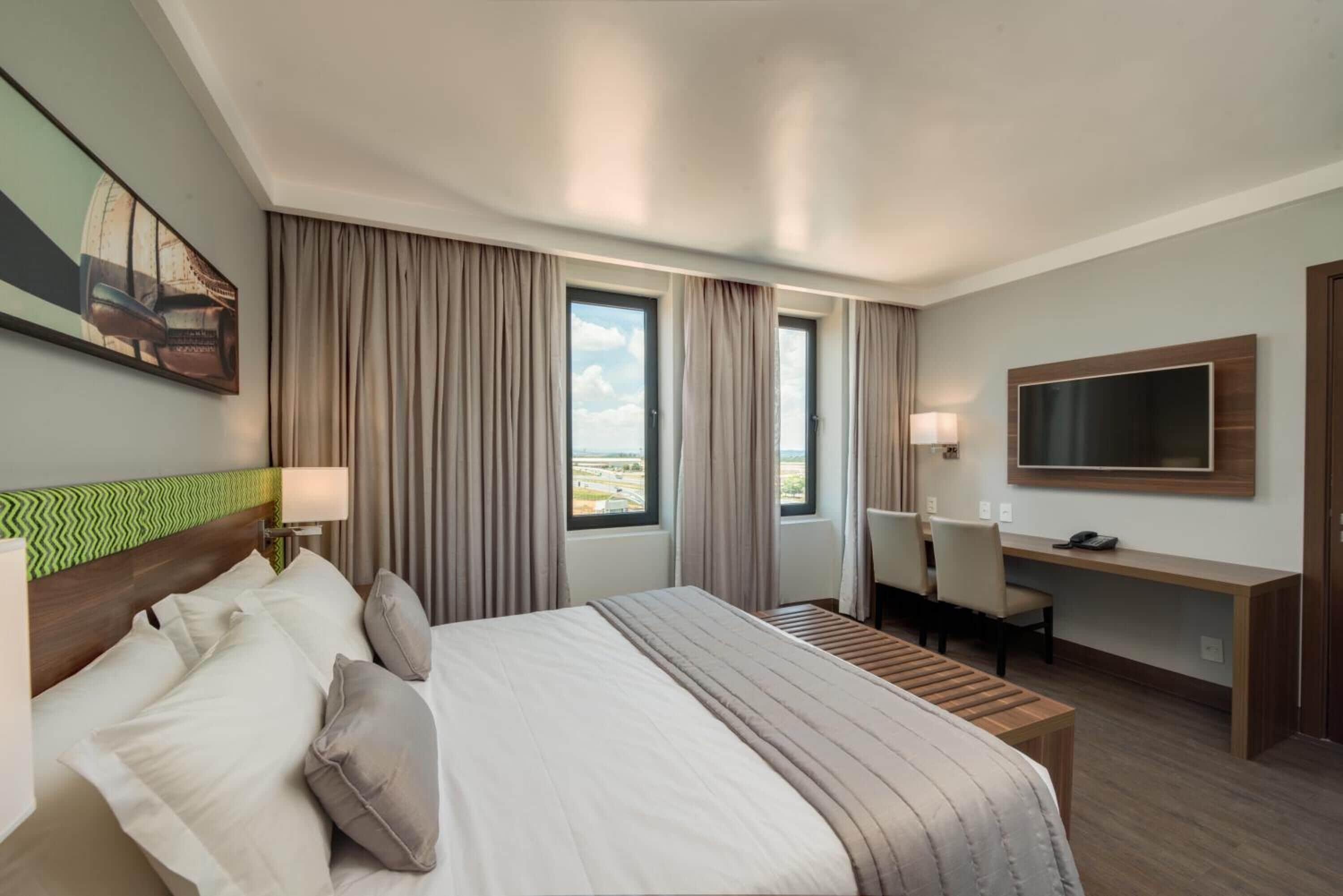 Habitación de hotel con una cama grande, un escritorio, un televisor y vistas al exterior.